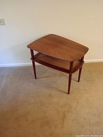Full view of the mid century end table showing the wooden top and wicker lower shelf with four tapered legs on carpet.