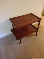Side angled view of the mid century wood bar cart, showing top tray with raised edges and bottom shelf with casters.