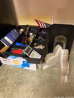 Photo showing drawer organizer filled with assorted office supplies, box of new file folders underneath, and metal bookends, small American flag behind