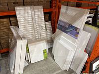 Shelf with stacks of wrapped stretched canvases and foamcore sheets