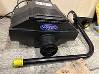 Front view showing the large convex lens and 'Prism Artograph' logo on the projector body with the attached black metal arm.