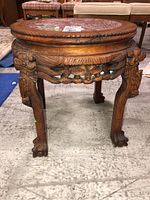 Full side view of a round wooden table with carved legs and stone top, showing overall condition and design.