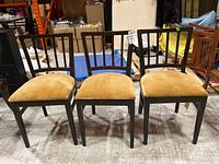 Set of three wooden chairs with mustard yellow upholstered seats, arranged side-by-side.