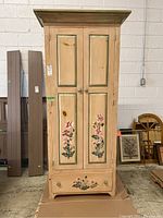 Full front view of the wooden cabinet showing two doors with floral painting and bottom drawer panel.