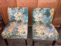 Front view of two matching floral fabric chairs side by side, showing full upholstery detail and dark wooden legs.