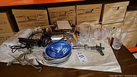 Photo of lot items on a wood surface with blue and white Royal Copenhagen plates, clear cut crystal glasses, metal garden tools, sprinkler, and picture frames visible.
