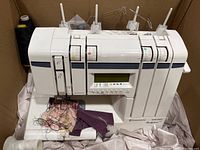 Frontal view of machine installed in shipping box showing scrap fabric and tangled threads