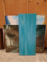 Four unframed original paintings arranged side by side against a wooden wall, showcasing various landscape and abstract art styles.