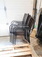 Six stacked outdoor chairs with synthetic woven wicker seats and backs and black metal frames, showing wear. Included for overall lot view.