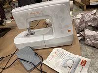 Front and side view of Huskystar by Husqvarna Viking ER10 sewing machine showing white body with leaf pattern, needle plate, and foot pedal.