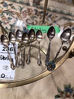 Nine sterling silver spoons arranged on glass table, visible wear and tarnish, with handwritten label 'Sterling'.