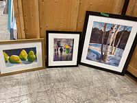 Three framed and matted watercolour paintings shown side by side: pears, rainy street, birch tree winter landscape.