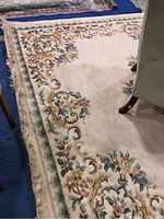 Photo of wool rug corner showing floral and scroll design on cream background with some soiling and wear.