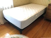 Twin bed frame with attached mattress near window and wooden floor
