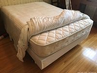 Bed with bedding folded back, showing mattress and box spring on a wooden floor