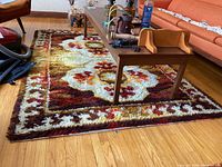 Shag carpet under a wooden coffee table with some objects; carpet shows floral pattern and colors.