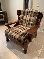 Wooden armchair angled view showing plaid cushioned seat and back, dark wood frame with carved armrests and legs.