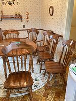 Group photo showing six wooden dining chairs around a dining table with a floral rug underneath. Four chairs, one armchair, and another chair visible.