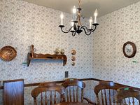 View of dining room corner with wooden chairs and table, pine wall shelf mounted, copper decorative plates on wall, and wooden oval clock.