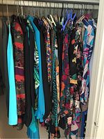 Photo of hanging vintage ladies clothing including blouses, dresses, and tops in assorted colors and patterns on rack.
