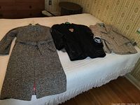 All three clothing items laid flat on bed: gray wool coat, black leather jacket, gray skirt suit jacket