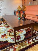 Side angle showing the entire rectangular wood coffee table with two antique-style lamps on top and an orange sofa in the background.
