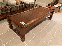 Side angle showing the coffee table's wooden frame, slatted top, rounded corners, and substantial legs.