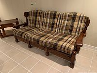 Front angle view of wood frame couch with plaid upholstered cushions, showing seat and back cushions as well as wooden arms and legs.