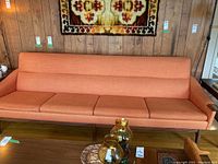 Full front view of orange fabric sofa against wood-paneled wall