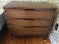 Front view of the medium wood tones mid-century modern dresser showing three drawers with recessed handle cutouts. Shows overall good condition with some visible scratches and wear.