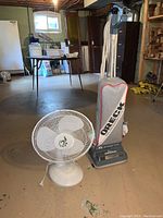 Photo showing the FC oscillating table fan and Oreck upright vacuum cleaner placed on a basement floor.