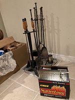 Two sets of fireplace tools and one box of StarterLog fire starter logs placed on basement floor near a cardboard box.