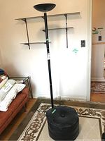 Full view of black metal torchiere lamp and black vinyl ottoman on rug in living room setting