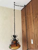 Full view of the hanging lamp suspended from the ceiling, showing the black metal chain and frame with amber glass shade underneath.
