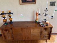 Long shot of brown wooden sideboard on which lamps, candle holders, and candles are arranged.