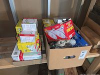 Two cardboard boxes containing multiple unopened boxes and loose light bulbs of various types, some packaging visible with GE and Sunbeam brands.