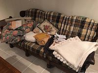 Overview of all mixed linens laid on patterned sofa including floral comforter, knitted throw, pillowcases, bedskirt, placemats and table linens.