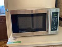 Front view of Hamilton Beach microwave showing stainless steel body, black glass door, and integrated handle.