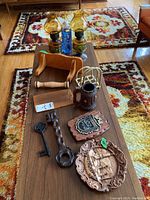 Full lot view with decorative oil lamps, pine shelf, wooden plaques, vintage keys, ceramic mug, and other German decorative items arranged on a wooden table.