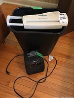 Image showing ShredMaster 40 shredder with white shred slot on top and black bin body, next to black Airworks space heater with control dials and power cord on wooden floor