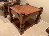 Wooden side table showing the carved legs, rounded finials, and lower shelf from an angled side view.