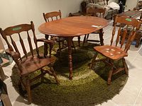 Full set of dining table with four chairs arranged on a green circular rug in basement setting.