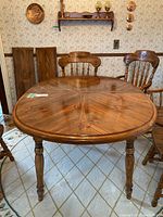 Full view of pine dining table with two leaves propped against wall behind chairs, showing table top and table legs.