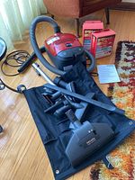 Overview of red canister vacuum, hose, wand, floor tool, accessories, manual, storage bag and boxed vacuum bags