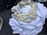 Photo of a stack of various used curtains in white and cream colors with metal grommets visible on one curtain.