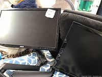 Photo showing two black ASUS monitors with adjustable stands on a couch and chair. Both screens are off.