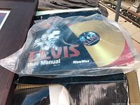 Elvis Karaoke machine user manual and gold record in plastic packaging, manual shows Elvis in black and white with red text, branded WowWee Live.