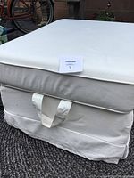 Photo of white fabric IKEA UPPLAND ottoman with washable cover, showing handle and clean fabric surface.