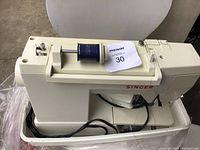 Cream-colored Singer sewing machine shown from top, with blue thread spool and Masoka tag on top surface.