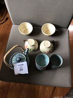 Blue ceramic teapot and 5 matching blue cups (inside stacked) and four fine china floral tea cups upside down on a chair.